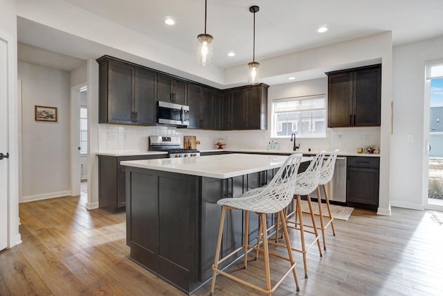 kitchen featuring dark brown cabinetry, stainless steel appliances, a kitchen island, hanging light fixtures, and light countertops