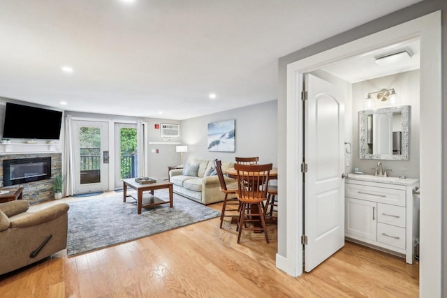 living room featuring a fireplace, sink, light hardwood / wood-style floors, and a wall unit AC