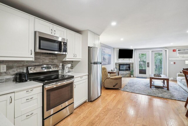 kitchen featuring appliances with stainless steel finishes, light hardwood / wood-style flooring, decorative backsplash, a wall unit AC, and white cabinetry