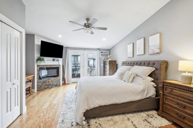 bedroom with light hardwood / wood-style flooring, access to outside, lofted ceiling, ceiling fan, and a fireplace