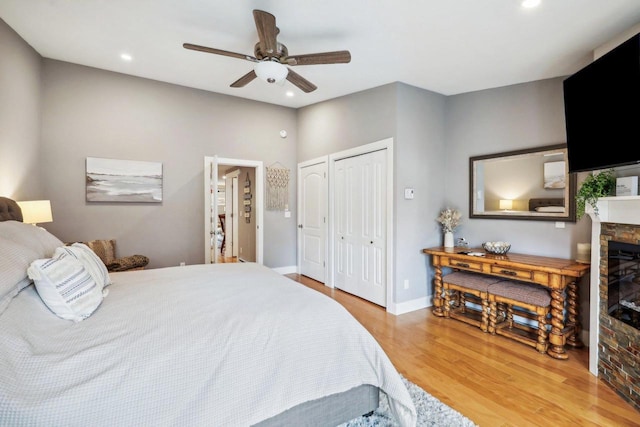 bedroom with ceiling fan, hardwood / wood-style floors, a stone fireplace, and multiple closets