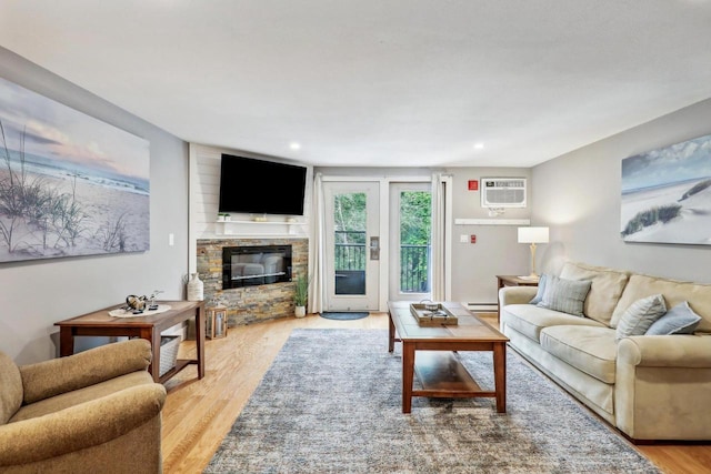 living room featuring a fireplace, baseboard heating, a wall mounted air conditioner, and light hardwood / wood-style flooring