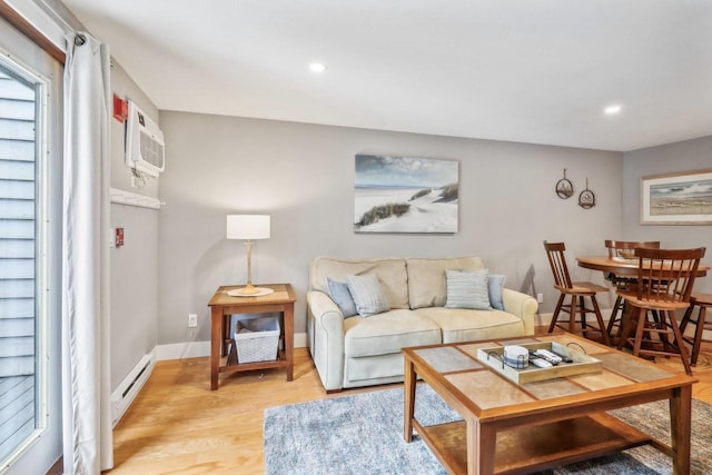 living room with a baseboard heating unit, a wall mounted AC, and light hardwood / wood-style floors