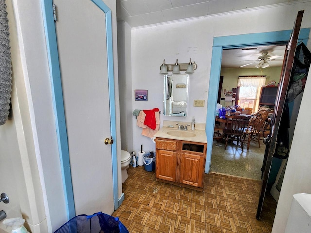 bathroom with toilet, vanity, parquet flooring, and ceiling fan