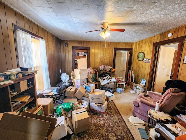 carpeted living room featuring ceiling fan and wood walls