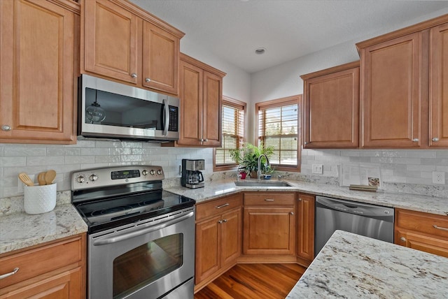 kitchen featuring brown cabinets, light stone counters, stainless steel appliances, and a sink