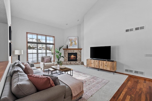 living room featuring high vaulted ceiling, a fireplace, visible vents, and wood finished floors