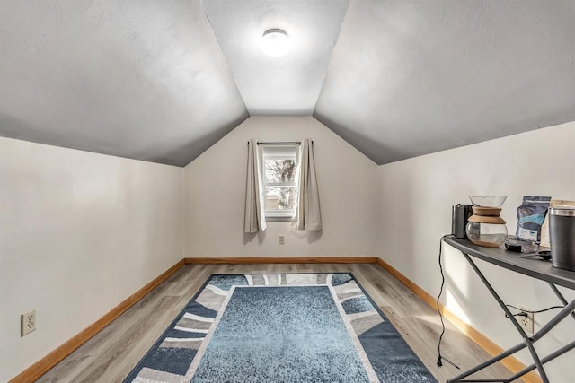 additional living space with light wood-type flooring, lofted ceiling, and a textured ceiling