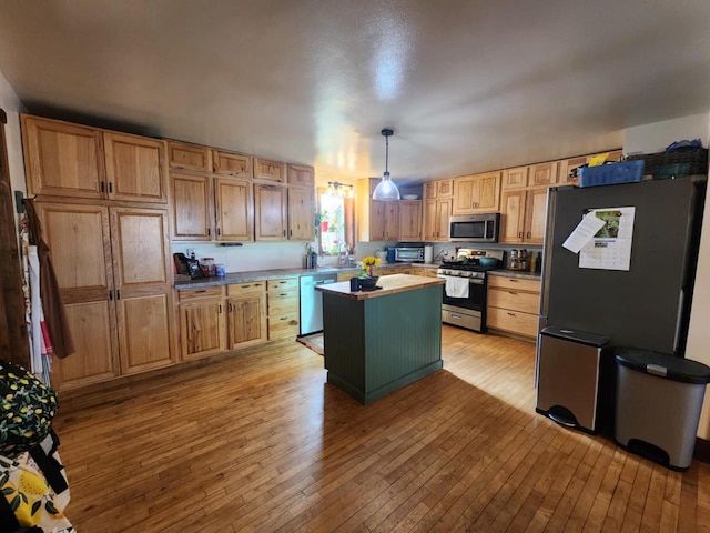 kitchen with pendant lighting, stainless steel appliances, a kitchen island, and light hardwood / wood-style flooring