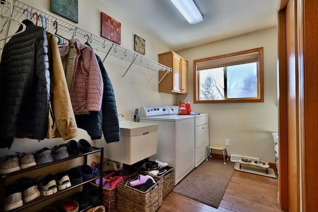 laundry room with sink, light wood-type flooring, washer and clothes dryer, and cabinets