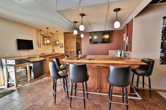 bar featuring butcher block countertops, hanging light fixtures, dark tile patterned floors, and a paneled ceiling