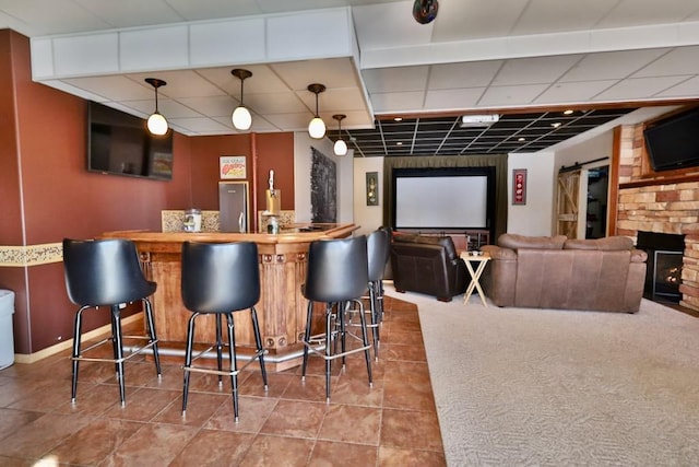 bar with tile patterned flooring, hanging light fixtures, a stone fireplace, and a paneled ceiling