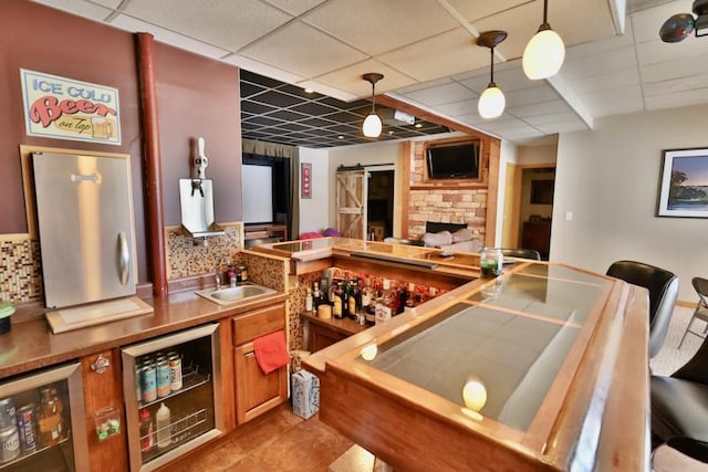 bar featuring hanging light fixtures, a barn door, sink, tasteful backsplash, and beverage cooler