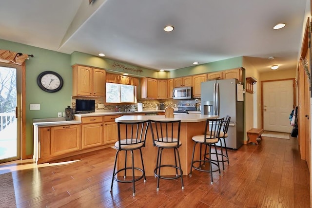 kitchen featuring hardwood / wood-style flooring, stainless steel appliances, a kitchen island, backsplash, and a kitchen bar