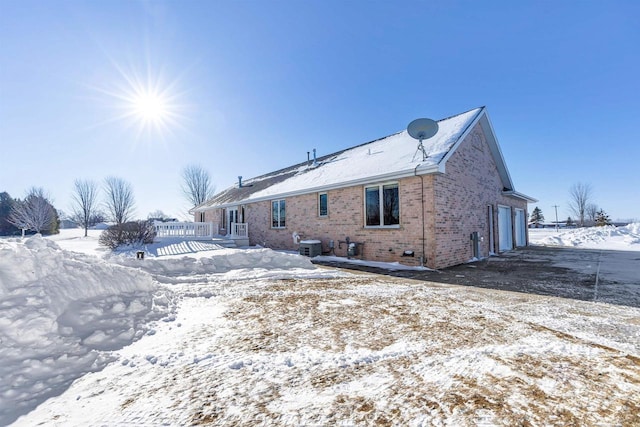 snow covered back of property featuring central AC unit and a garage