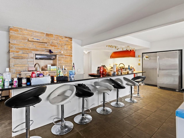 kitchen with a kitchen breakfast bar, sink, dark tile patterned flooring, and stainless steel refrigerator