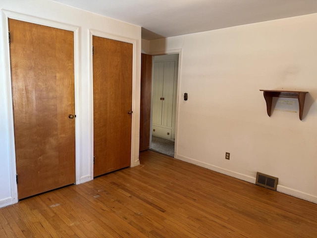 unfurnished bedroom featuring light hardwood / wood-style flooring and two closets