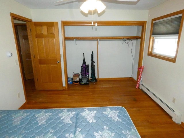 unfurnished bedroom featuring ceiling fan, a closet, a baseboard heating unit, and hardwood / wood-style floors