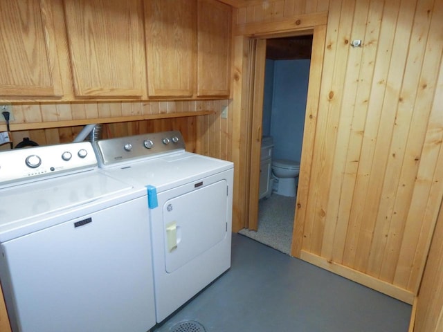 laundry area with washing machine and clothes dryer, wood walls, and cabinets