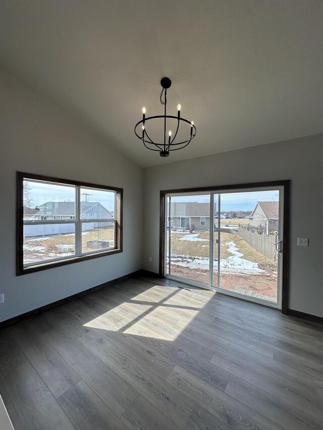 empty room with a chandelier, a healthy amount of sunlight, lofted ceiling, and wood finished floors