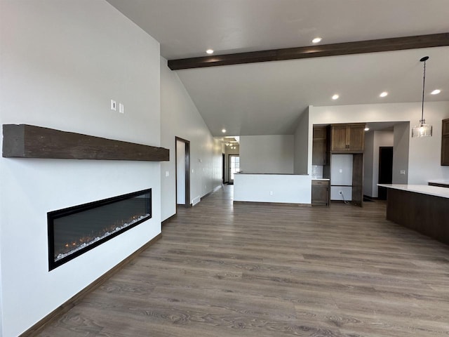 unfurnished living room featuring baseboards, dark wood finished floors, lofted ceiling with beams, recessed lighting, and a glass covered fireplace