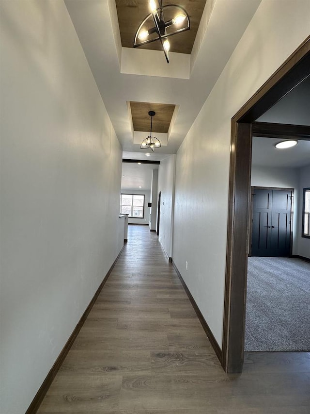 hall featuring a tray ceiling, wood finished floors, baseboards, and a chandelier