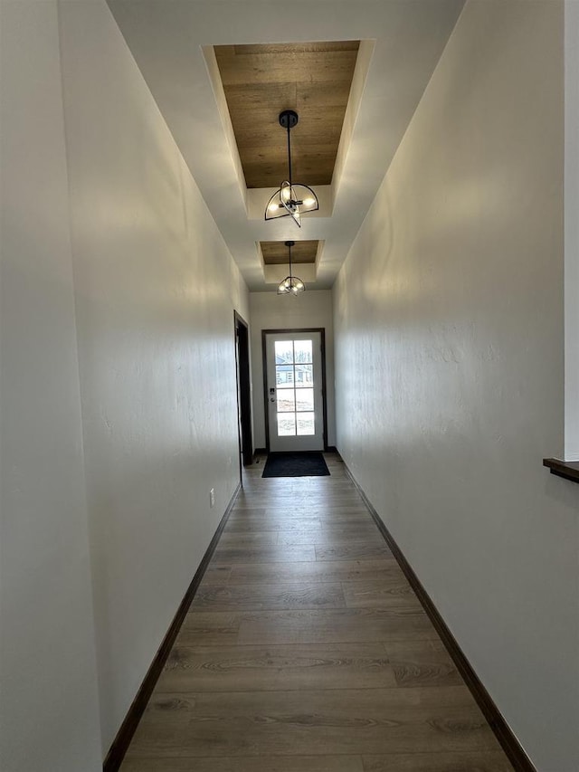 doorway featuring a tray ceiling, wood finished floors, baseboards, and wooden ceiling