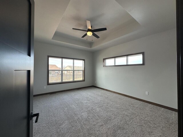 empty room with a tray ceiling, baseboards, and carpet