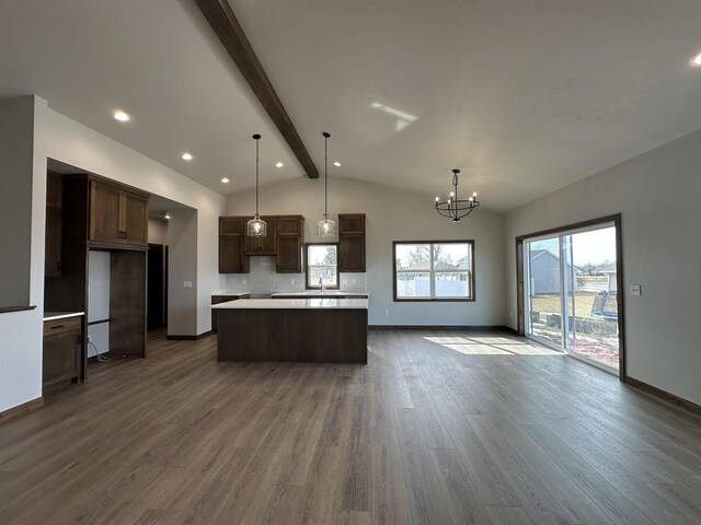 kitchen with dark wood-type flooring, lofted ceiling with beams, tasteful backsplash, a kitchen island, and an inviting chandelier