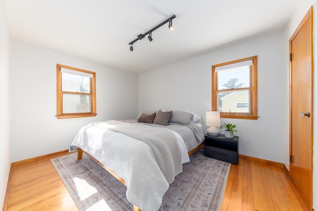 bedroom with multiple windows, light hardwood / wood-style flooring, and track lighting