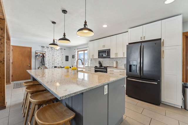 kitchen featuring an island with sink, light stone counters, pendant lighting, black refrigerator with ice dispenser, and white cabinetry