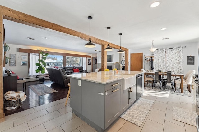 kitchen featuring a center island with sink, stainless steel dishwasher, decorative light fixtures, gray cabinets, and sink