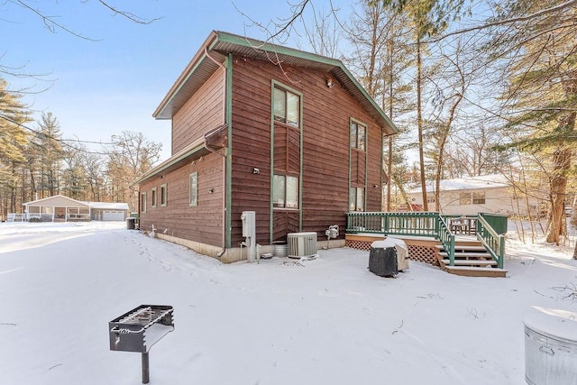 snow covered house with cooling unit and a wooden deck