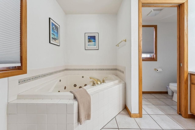 bathroom with a relaxing tiled tub, toilet, and tile patterned floors