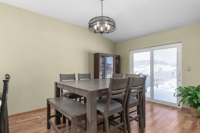 dining space with light hardwood / wood-style floors, a chandelier, and vaulted ceiling