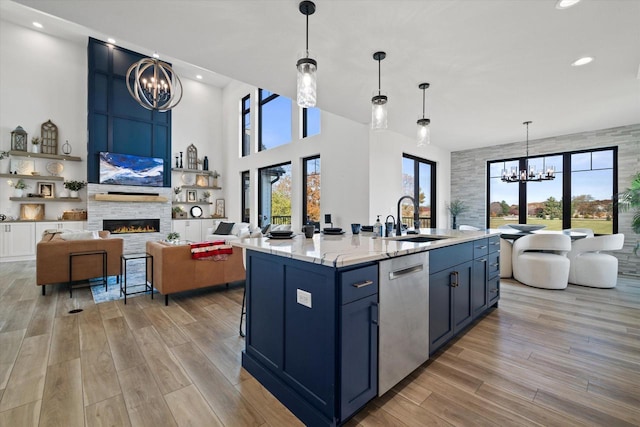 kitchen featuring a center island with sink, a stone fireplace, sink, dishwasher, and a chandelier