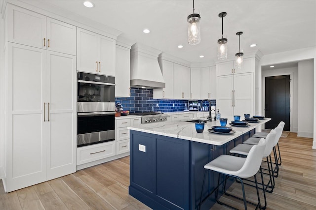 kitchen with appliances with stainless steel finishes, an island with sink, light stone countertops, white cabinets, and custom exhaust hood