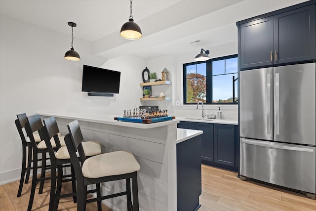 bar with blue cabinetry, stainless steel fridge, light hardwood / wood-style floors, and decorative light fixtures