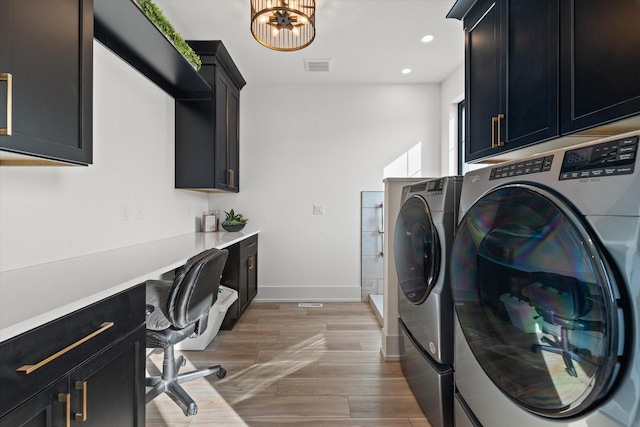 clothes washing area featuring light hardwood / wood-style floors, a chandelier, washer and clothes dryer, and cabinets