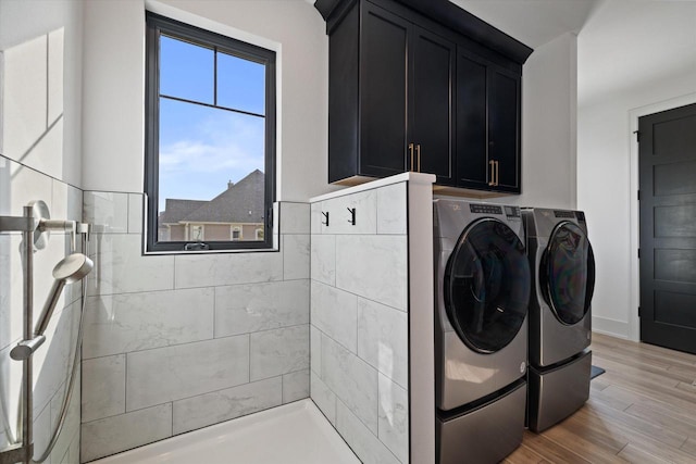 washroom with washing machine and clothes dryer, cabinets, and light hardwood / wood-style flooring