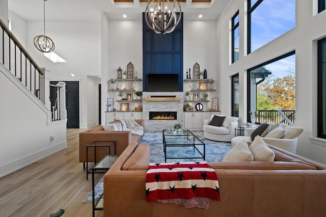 living room featuring light hardwood / wood-style floors, an inviting chandelier, a stone fireplace, and a high ceiling