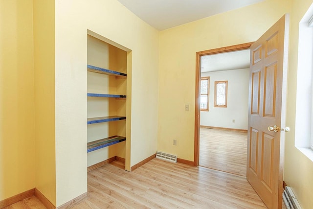 hall featuring baseboards, baseboard heating, visible vents, light wood-style floors, and built in shelves