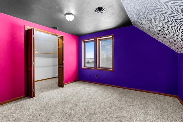 additional living space with a textured ceiling, vaulted ceiling, and light colored carpet