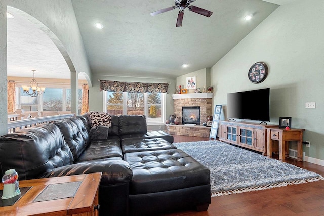 living room featuring ceiling fan with notable chandelier, high vaulted ceiling, a stone fireplace, and wood-type flooring