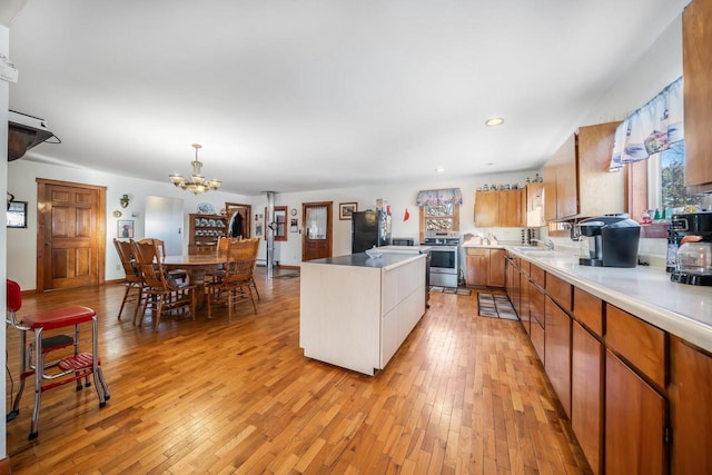 kitchen featuring light wood-type flooring, black refrigerator, stainless steel stove, sink, and pendant lighting