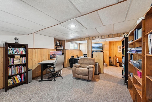 office space with carpet, a drop ceiling, and wood walls