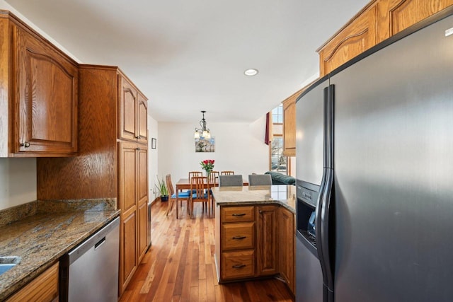 kitchen with appliances with stainless steel finishes, hardwood / wood-style floors, stone countertops, and decorative light fixtures