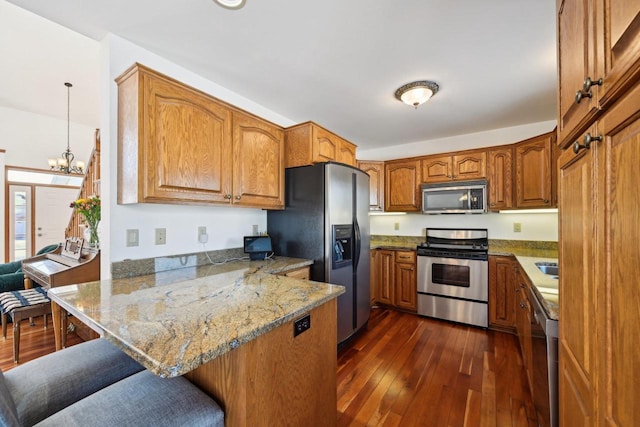 kitchen with kitchen peninsula, stainless steel appliances, decorative light fixtures, dark wood-type flooring, and a kitchen breakfast bar