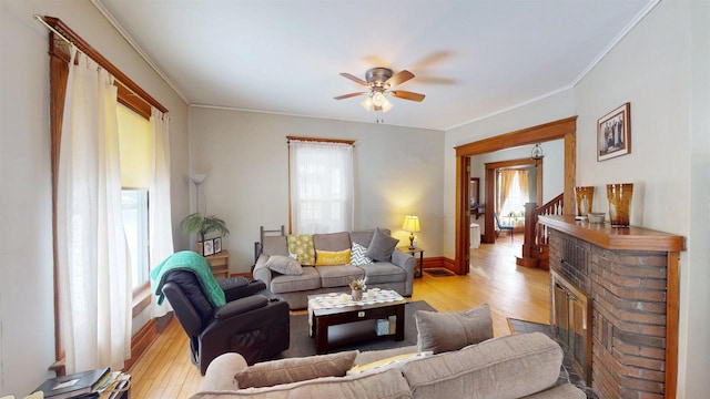 living room with ceiling fan, light hardwood / wood-style flooring, crown molding, and a brick fireplace