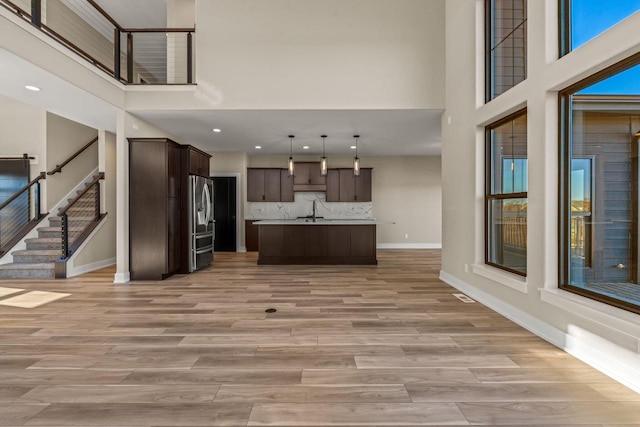 unfurnished living room with sink, a towering ceiling, and light hardwood / wood-style flooring